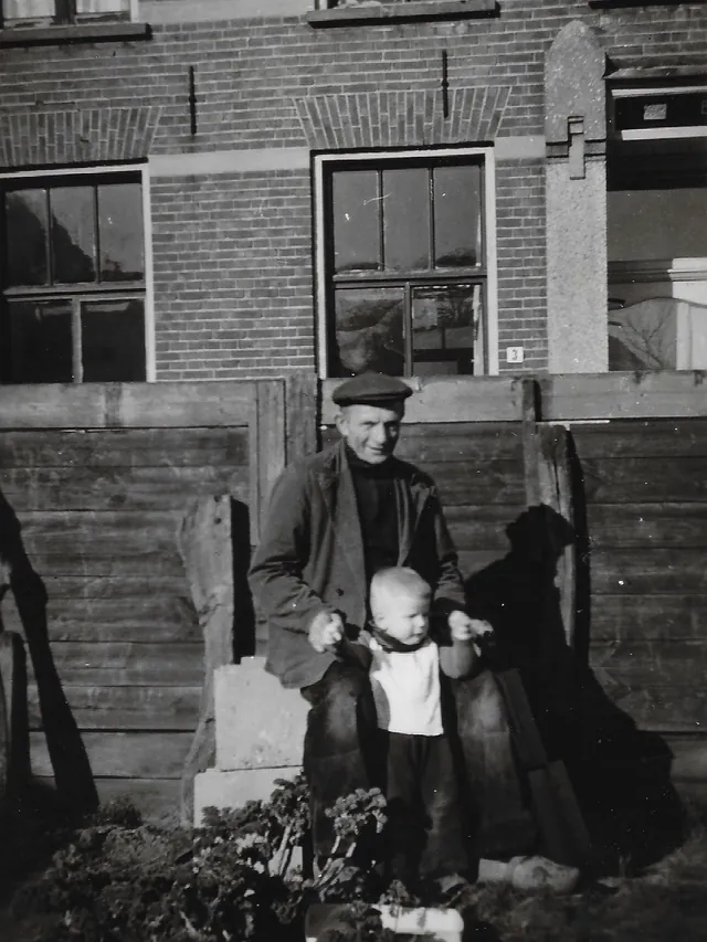 De mandenmaker met een kleinkind achter de zaak